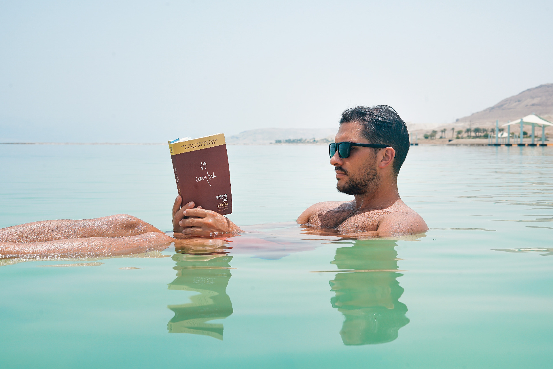 Man relaxing sitting in the sea reading a book.